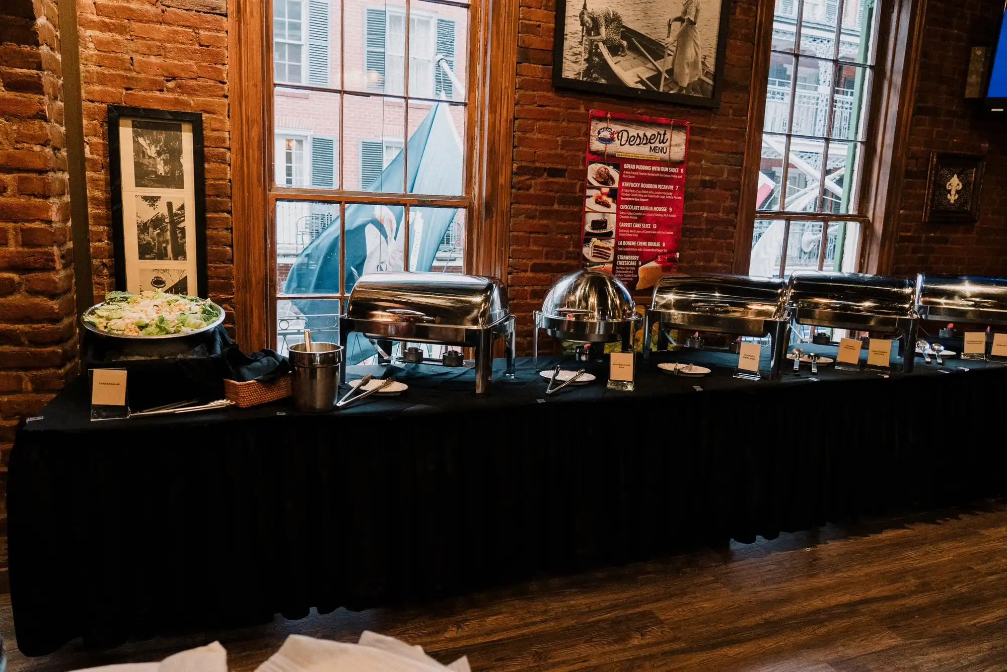 A catering buffet of chafing dishes set up along a brick wall
