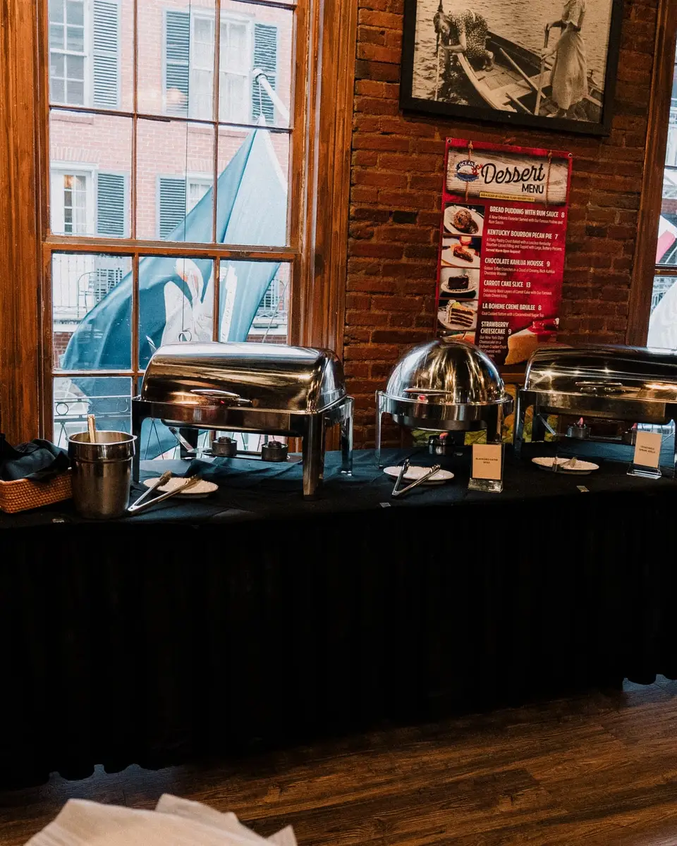 A catering buffet of chafing dishes set up along a brick wall