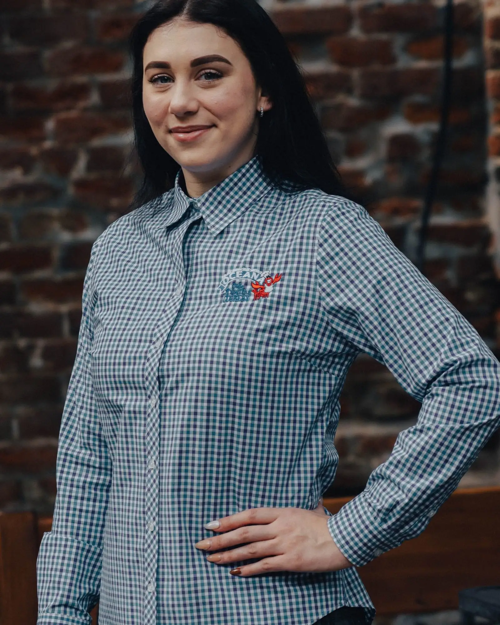 A woman wearing the gingham Oceana button-up shirt with the embroidered logo