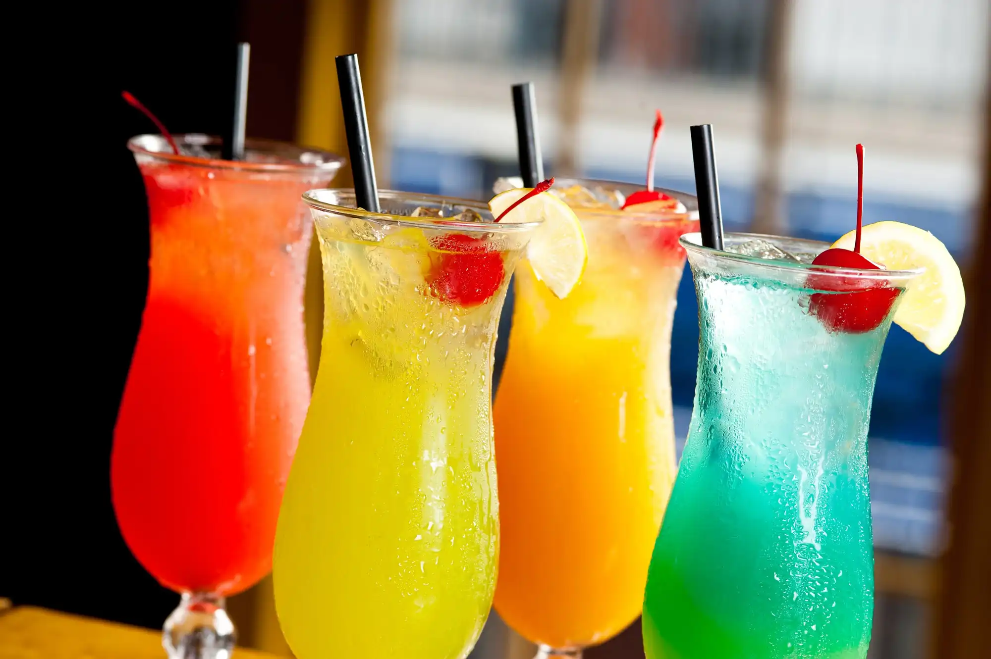 Four tropical cocktails in hurricane glasses, red, yellow, orange and blue