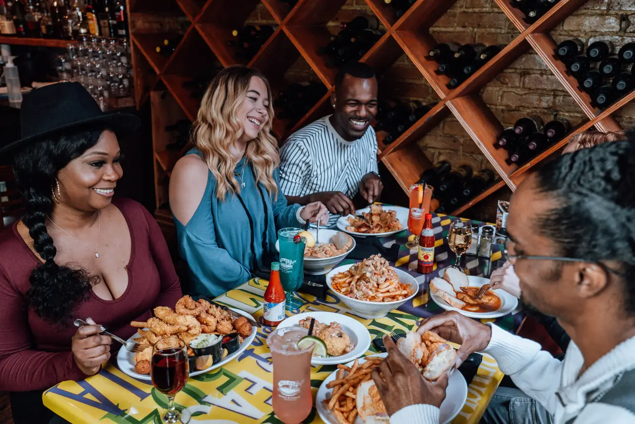 A group laughing over dinner at a colorful table in front of Oceana’s wine wall