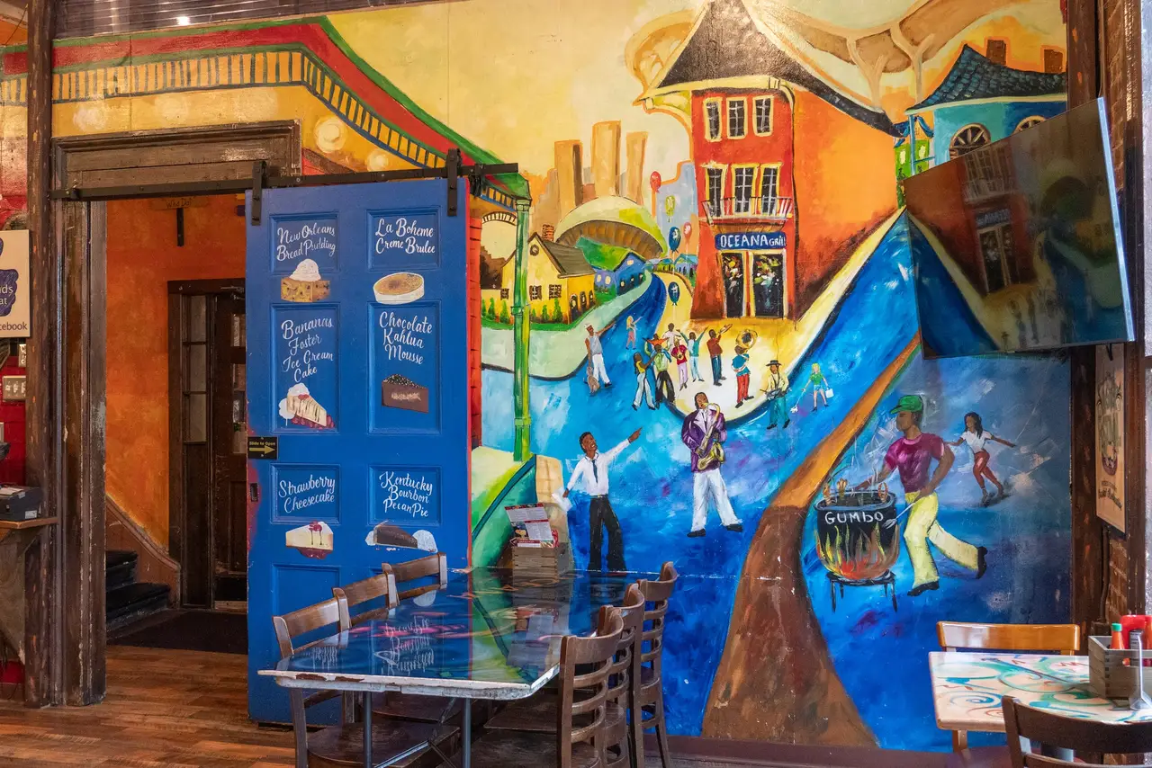 A colorful mural of a New Orleans street parade covering a wall of the La Bohème Room