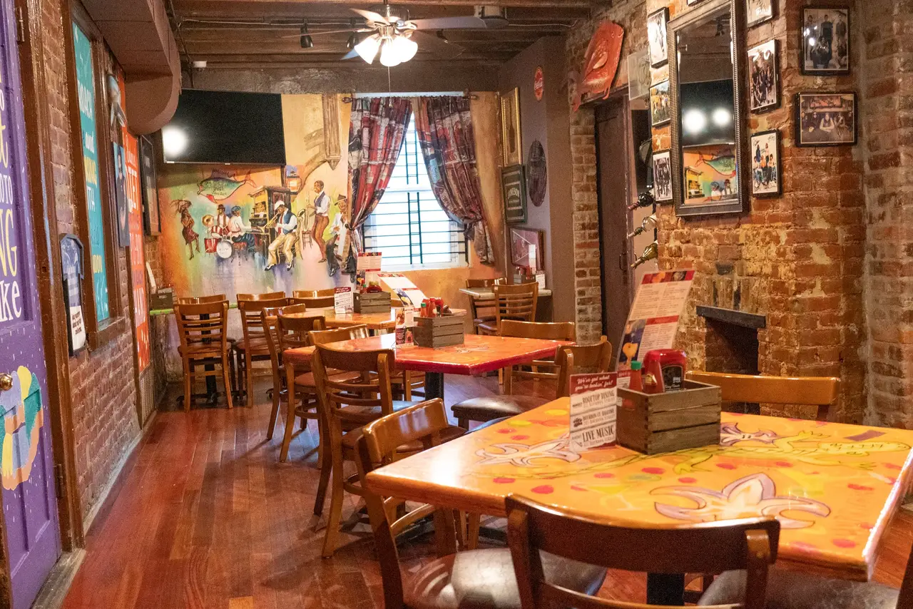 The Tchoupitoulas Room: colorful New Orleans signs and art on brick walls, with tables down the room